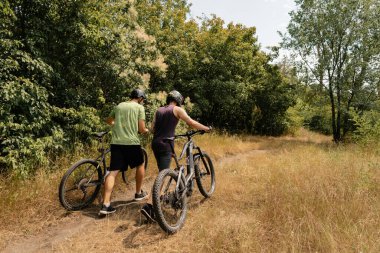 Two people stand beside mountain bikes in a forest trail enjoying outdoor activities