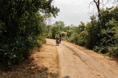 Two people riding bicycles through a dirt path surrounded by lush greenery
