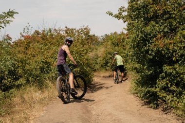 Cyclists exploring a scenic dirt path bordered by vibrant greenery under a sunny sky