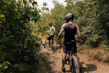 Two men riding bicycles on a natural path surrounded by greenery and trees