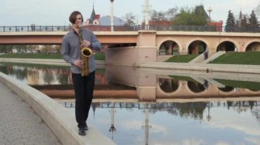 genç adam saksafon çalıyor. 4 k. müzisyen Nefesli/Üflemeli Saz üzerinde çalış, yürüyüşler parapet kamera, kamera için harekete geçti. Adam dar yolda taşır. adam arka plan şehrin üzerinde
