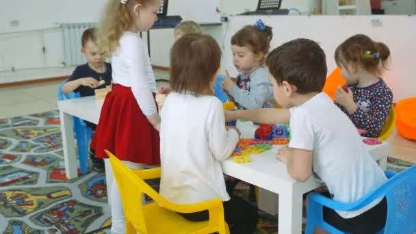 I bambini stanno sviluppando una sala giochi. Emozioni dei bambini durante le lezioni divertenti. I bambini costruiscono edifici con figure geometriche in plastica e legno . — Video Stock