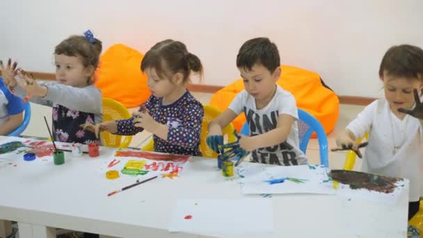 Childrens developing a game room. Emotions of young children during entertaining classes. children paint with finger paints on white sheets of paper. children stretch their hands in the paint smeared — Stock Video