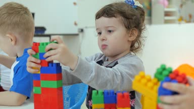 Çocuk oyun odası. Küçük çocukların duygu eğlence etkinlikleri sırasında. Erkek ve kız masada oturan çok renkli plastik Legolarla oynamak. kız burnunu çizikler dokunduğundan