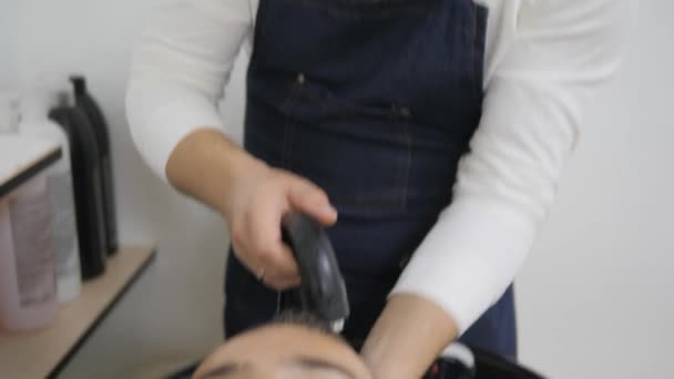 Peluquería para hombres. Barbería. Un joven recibe un corte de pelo y un servicio de cuidado del cabello de un hombre barbudo con un cabello atado a la cabeza. Lavando la cabeza de los clientes con detergentes. ducha humedece la cabeza — Vídeos de Stock