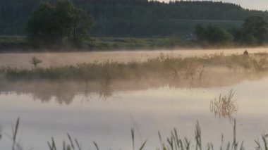 Güneş doğuyor. Sabah manzara. Sabah gökyüzüne ve nehir sulu yüzeyi onun yansıması. Yaz sabahı. Sis Nehri. Balıkçı siluet uzaktan şişme bir teknede. 4k