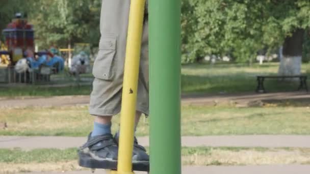 Gymnases d'exercice en plein air. enfant a un simulateur. Jambes en sandales balançoire sur un pendule . — Video
