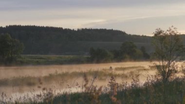 Güneş doğuyor. Sabah manzara. Sabah gökyüzüne ve nehir sulu yüzeyi onun yansıması. Yaz sabahı. Sis Nehri. Balıkçı siluet uzaktan şişme bir teknede