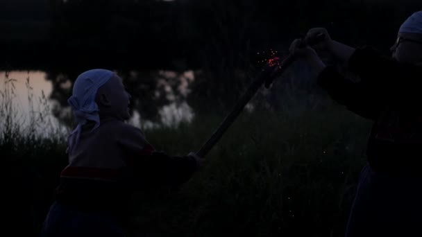 Chispas de palos ardiendo. Batalla de niños a dubankah ardiente. niños luchan contra el fondo del río. Las brasas de los palos ardientes se dispersan en diferentes direcciones. Movimiento lento — Vídeos de Stock