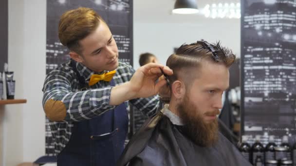 Cabeleireiro para homens. Barbearia. Cabeleireiro com um corte de cabelo funciona para um penteado para um cara barbudo. O conceito de um estilo de vida hipster. Cabeleireiro corte de cabelo com unhas na cabeça dos clientes. Cliente — Vídeo de Stock