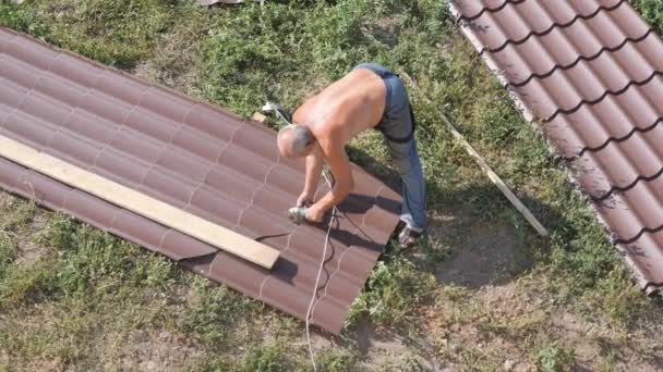 Jobbar med takmaterialet. tak av metall. Skära profil metall elektriska bulgariska. Gnistor från under metall cirkeln av hand skärverktyget. ark av takmaterial ligger på grönt gräs — Stockvideo