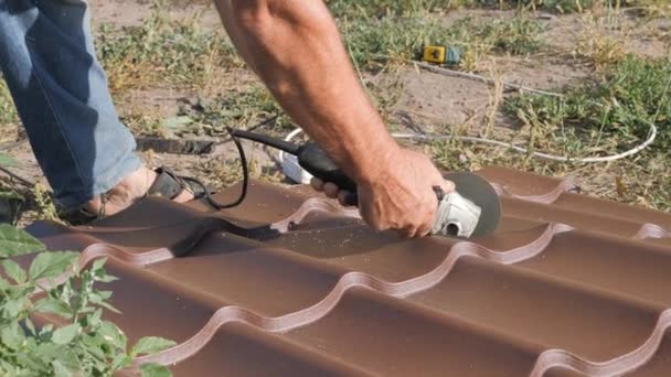 Work with roofing material. roof of metal. Cutting profile metal electric bulgarian. Sparks fly from under the metal circle of the hand cutting tool. sheet of roofing material lies on green grass — Stock Video