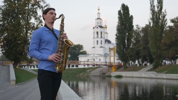 Saxofonista toca trompete. City Embankment. um homem com bigode a tocar um instrumento musical nas ruas da cidade . — Vídeo de Stock