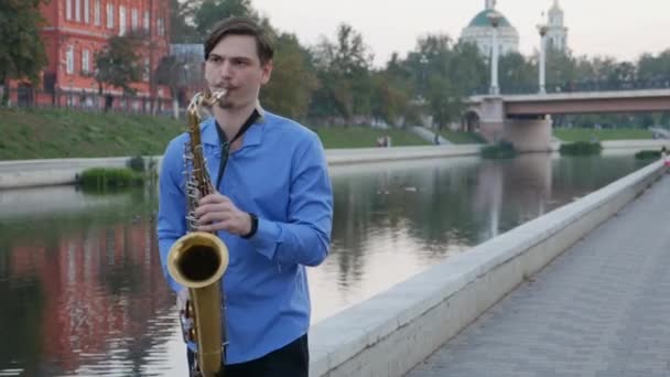 Saxofonista toca trompete. City Embankment. um homem com bigode a tocar um instrumento musical nas ruas da cidade. saxofone Linton — Vídeo de Stock