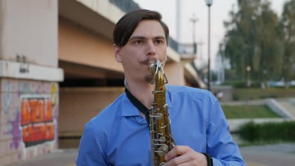 El saxofonista toca la trompeta. City Embankment. un hombre con bigote batido tocando un instrumento musical en las calles de la ciudad. músico toca un instrumento musical bajo el puente . — Vídeos de Stock