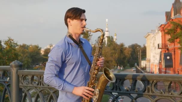 Saxofonist speelt de trompet. Stad Embankment. man met een muricola omhoog snor die een muziekinstrument spelen op de straten van de stad. muzikant staat op de brug en speelt een muziekinstrument. — Stockvideo