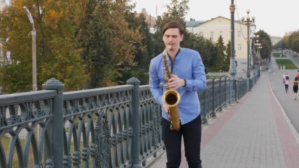 Saxophonist plays the trumpet. City Embankment. man with a whiskered up mustache playing a musical instrument on the streets of the city. musician stands on the bridge and plays a musical instrument. — Stock Video