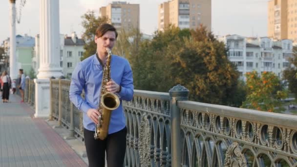 Saxofonista toca trompete. City Embankment. um homem com bigode a tocar um instrumento musical nas ruas da cidade. músico fica na ponte e toca um instrumento musical . — Vídeo de Stock