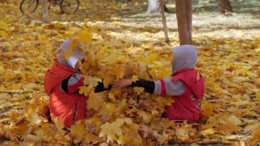 Sonbahar. Sarı yapraklar küçük çocuklarda. Çocuklar sokakta düşen yapraklar ile oynamak. Sonbahar grove ağaç ve maples. Çocuklar kadar düşen yapraklar ağaçların üst atmak. Çocuklar arasında oturmak