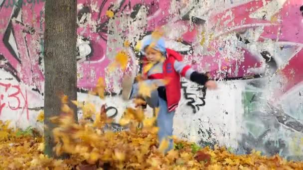 Jesienią. Małe dzieci w żółte liście. Dzieci bawią się w ulicy z opadłych liści. Jesienne grove brzóz i klony. Szczęśliwy kids na ulicy. chłopak idzie przez fallen jesieni — Wideo stockowe