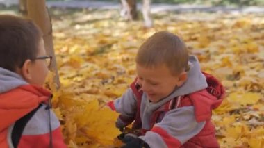 Sonbahar. Sarı yapraklar küçük çocuklarda. Çocuklar sokakta düşen yapraklar ile oynamak. Sonbahar grove ağaç ve maples. Çocuklar kadar düşen yapraklar ağaçların üst atmak. Çocuklar arasında oturmak