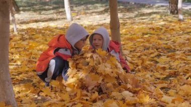 Sonbahar. Sarı yapraklar küçük çocuklarda. Çocuklar sokakta düşen yapraklar ile oynamak. Sonbahar grove ağaç ve maples. Çocuklar kadar düşen yapraklar ağaçların üst atmak. Çocuklar arasında oturmak