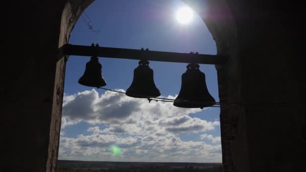 Glocken auf dem Hintergrund des blauen Himmels mit Wolken. Glocken in verschiedenen Größen hängen in einem Ziegelbogen in großer Höhe. — Stockvideo
