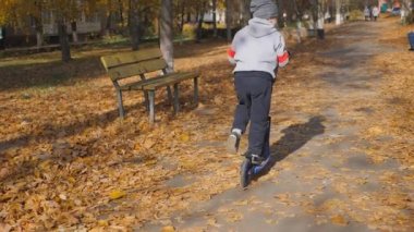 Çocuk bir scooter sürme. küçük çocuk ayaklarıyla itiyor ve tahta üzerinde sürmek. Çocuk direksiyonu tutan ve bir scooter sürme. Spor, yavaş çekim
