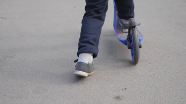 Çocuk bir scooter sürme. Çocuk ayak asfalt iter ve tahta üzerinde duruyor. çocuk ile bir scooter gemide gidiyor. yavaş çekim