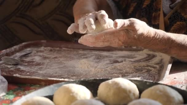 Las manos de las abuelas hacen pasteles. Las manos femeninas arrugadas enrollan bolas de masa. Amasar la masa en la cocina casera . — Vídeos de Stock