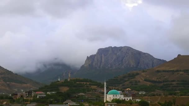 Montanhas no fundo de nuvens cinzentas. Nuvens escuras envolvem os cumes das montanhas. melhores tipos de cadeias de montanhas. Bela vista das montanhas. melhor vídeo de penhascos íngremes. Mesquita antiga em — Vídeo de Stock