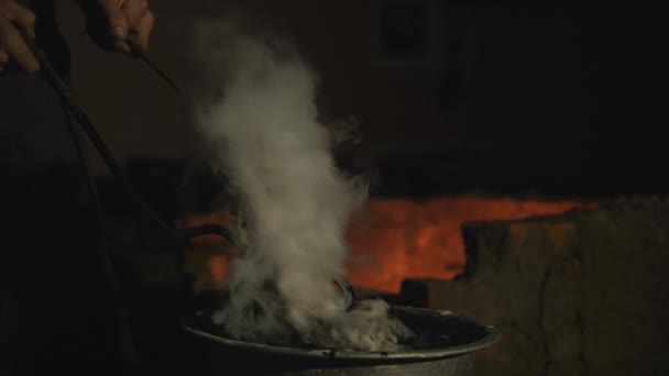 Schmied bearbeitet Metall. Handwerker, der Hochländer auf Privatschmiede im Dorf. Verhärtung von Metallprodukten. Warmes Produkt in einem Behälter mit kaltem Öl baden. Öl raucht weißen Rauch aus dem — Stockvideo