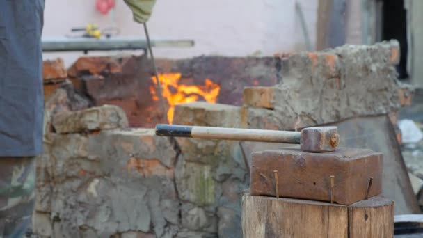 Fabbro lavora metallo. Artigiano, l'Highlander su fucina privata nel villaggio. mazza giace sull'incudine. Master interferisce con carbone in un forno caldo, crogiolo . — Video Stock