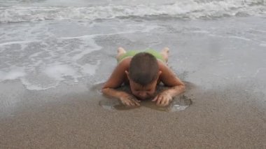 kumlu sahilde dalgalar deniz onun karnına çocuk yatıyor. Sahilde kum kürek çocuk. Dalgalar deniz yıkanmış çocuk.