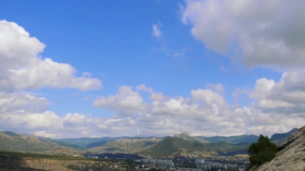 Fortaleza genovesa, Sudak, Crimeia. Montanhas contra o céu azul com nuvens brancas. As nuvens circulares atravessam o céu azul. Vista superior da cidade nas montanhas, os edifícios e a estrada com passagem — Vídeo de Stock