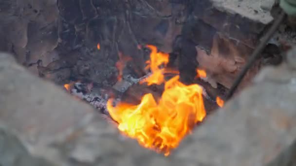 Ferreiro trabalha metal. Artesãos, os Highlander em ferreiros privados na aldeia. A queimar troncos na fornalha dos ferreiros. Tirando o tarugo quente quente da lareira usando carrapatos. Faíscas voam — Vídeo de Stock