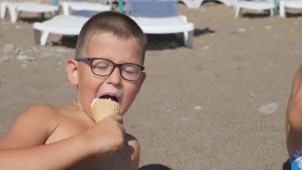 Το παιδί τρώει παγωτό. αγόρι αλείψει το πρόσωπό του με το φαγητό. Το παιδί τρώει παγωτό από ένα χωνάκι βάφλα. — Αρχείο Βίντεο