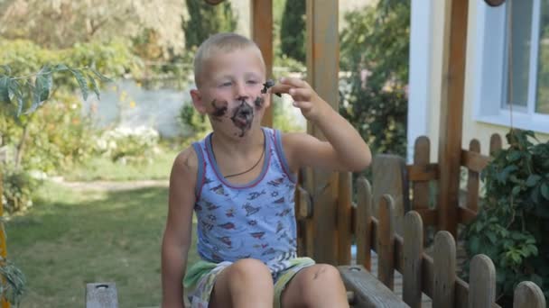 A criança come gelado. O rapaz sujou a cara com comida. Criança comendo sorvete de um cone de waffle preto . — Vídeo de Stock