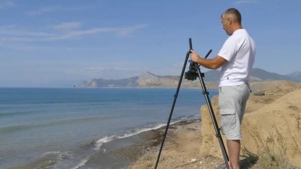 Videógrafo dispara la costa en una cámara montada en un trípode — Vídeo de stock