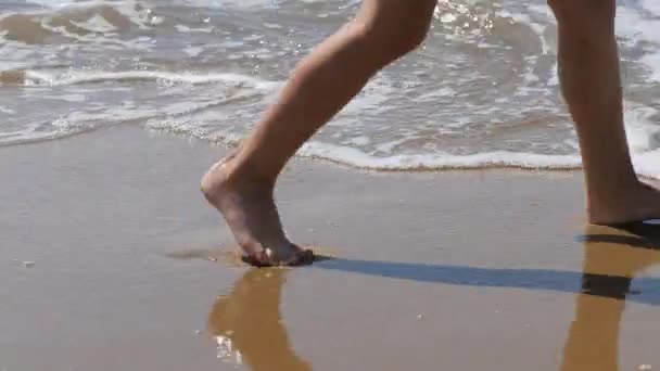 Child goes along the surf. Childrens feet on the background of waves. sea water washes away the footprint — Stock Video