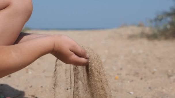 子供は、浜辺の砂をばらまきます。子供手一握りの砂をすくって、上部に発生、ビーチで彼の指を注ぐ. — ストック動画