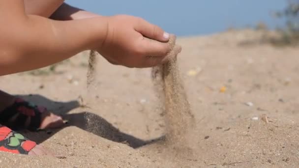 子供は、浜辺の砂をばらまきます。子供手一握りの砂をすくって、上部に発生、ビーチで彼の指を注ぐ. — ストック動画