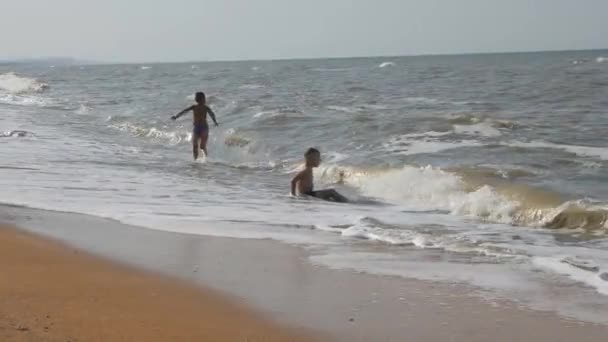 婴儿在海滩上 在海上的浪潮 两个男孩在金色的沙滩上在海浪中玩耍 挥动与头覆盖的孩子 完整的高清 — 图库视频影像