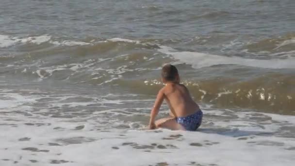 Baby na plaży, w morskich fal. chłopiec na złotym piasku, grając w surf. fala z głowy obejmuje dziecko. — Wideo stockowe