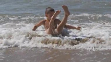 baby on the beach, in the maritime wave. boy on the golden sand playing in the surf. wave with the head covers the child.