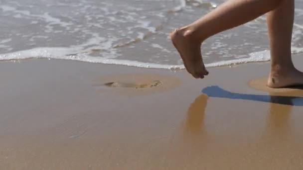 Kind gaat langs de branding. Childrens voeten op de achtergrond van de golven. zeewater wegspoelt de voetafdruk. — Stockvideo