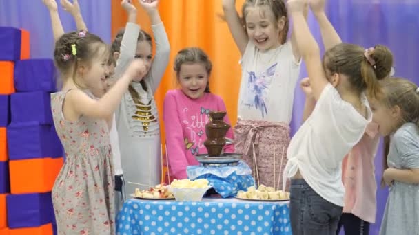 Sala de juegos para niños. Los niños comen chocolate de una fuente de chocolate . — Vídeo de stock