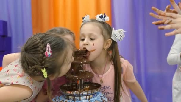 Sala de juegos para niños. Los niños comen chocolate de una fuente de chocolate . — Vídeo de stock