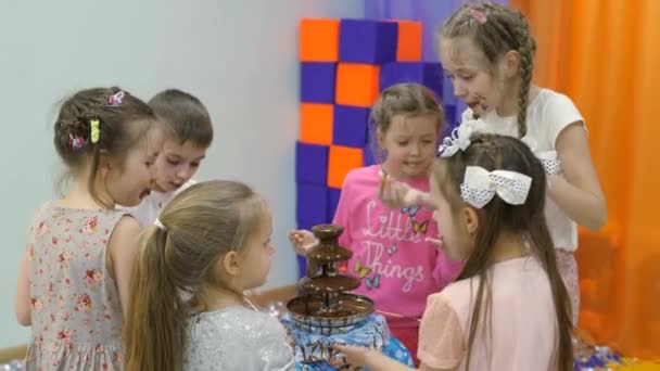 Childrens speelkamer. Kinderen eten chocolade van een fontein van de chocolade. — Stockvideo