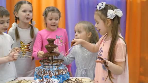 Sala de jogos das crianças. As crianças comem chocolate de uma fonte de chocolate . — Vídeo de Stock